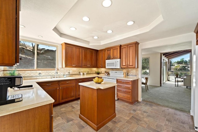 kitchen featuring a raised ceiling, sink, white appliances, a center island, and carpet floors