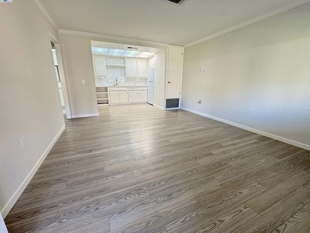 unfurnished living room featuring sink, ornamental molding, and light wood-type flooring