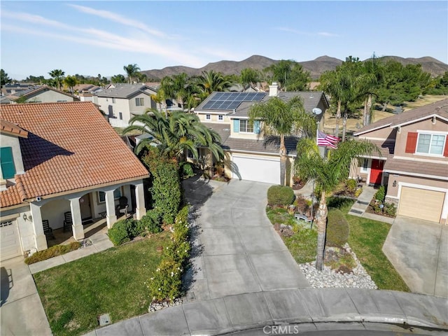 view of front of home featuring covered porch, a garage, a mountain view, a front yard, and solar panels