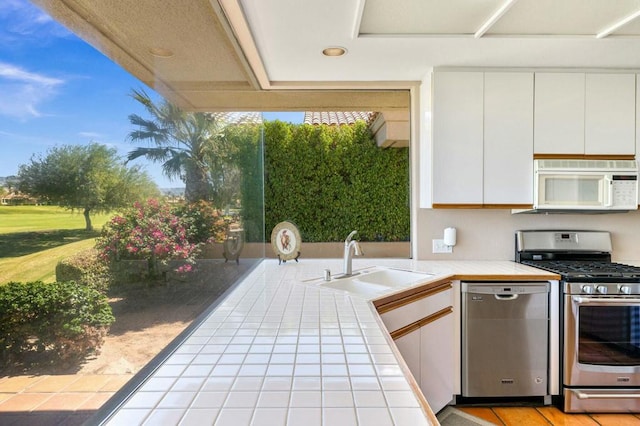 kitchen with white cabinets, tile counters, stainless steel appliances, sink, and light tile patterned floors