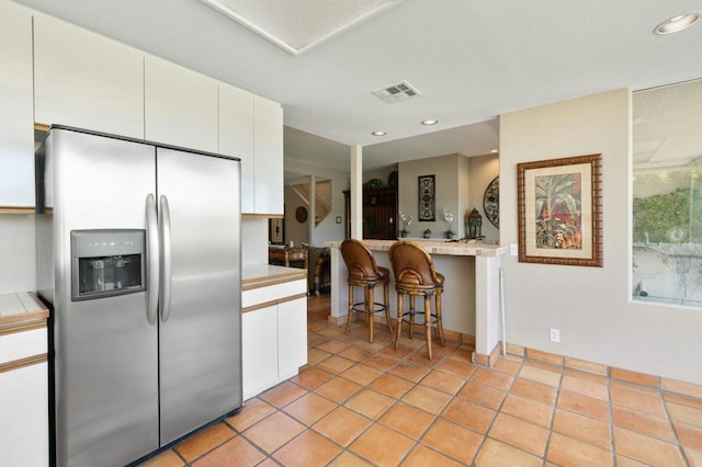 kitchen featuring white cabinets, a breakfast bar area, stainless steel fridge with ice dispenser, and light tile patterned floors