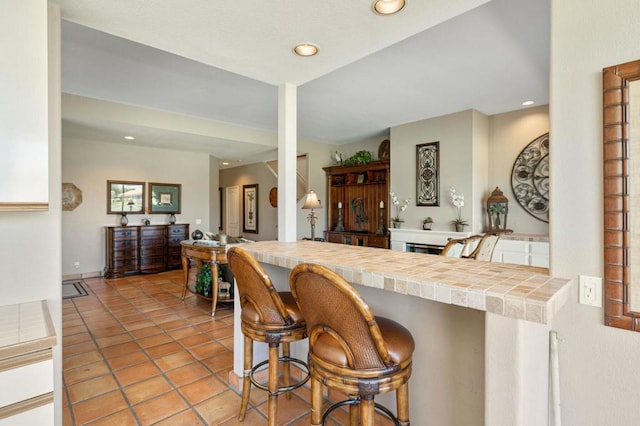 kitchen with a breakfast bar area, kitchen peninsula, tile counters, and light tile patterned flooring