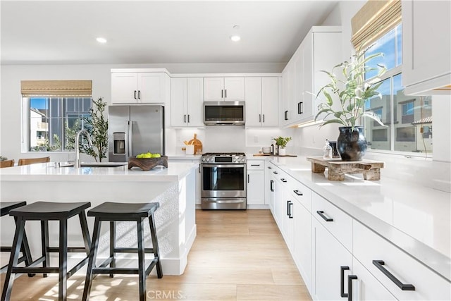 kitchen featuring white cabinets, stainless steel appliances, sink, a kitchen breakfast bar, and light wood-type flooring