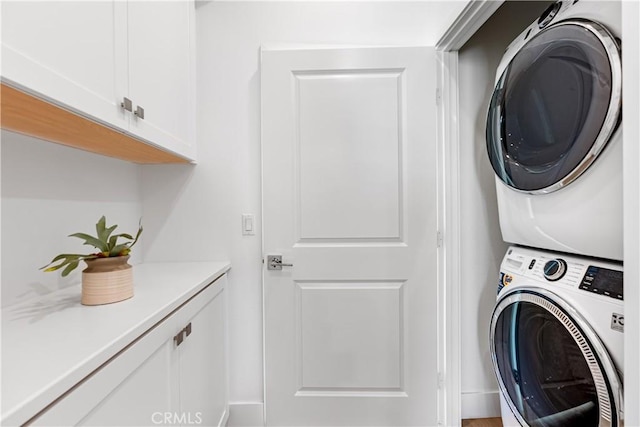 laundry room featuring cabinets and stacked washer / dryer