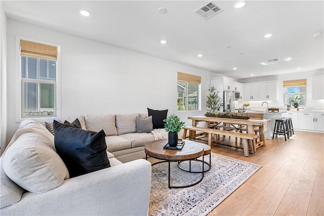 living room featuring sink, light wood-type flooring, and a healthy amount of sunlight