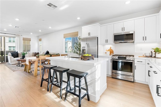 kitchen with white cabinets, stainless steel appliances, an island with sink, sink, and a breakfast bar