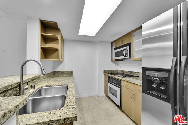 kitchen with light stone counters, stainless steel appliances, a skylight, and sink