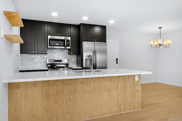 kitchen with pendant lighting, stainless steel appliances, backsplash, light stone counters, and light hardwood / wood-style flooring