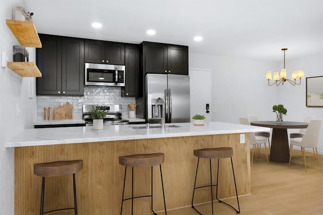 kitchen featuring a kitchen breakfast bar, appliances with stainless steel finishes, light wood-type flooring, light stone countertops, and decorative backsplash