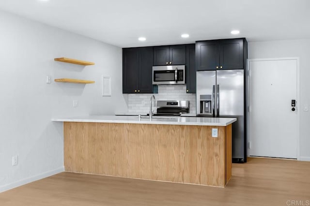 kitchen with decorative backsplash, appliances with stainless steel finishes, light hardwood / wood-style flooring, and kitchen peninsula