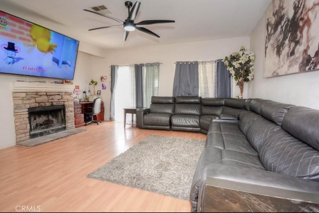 living room with a stone fireplace, hardwood / wood-style floors, and ceiling fan