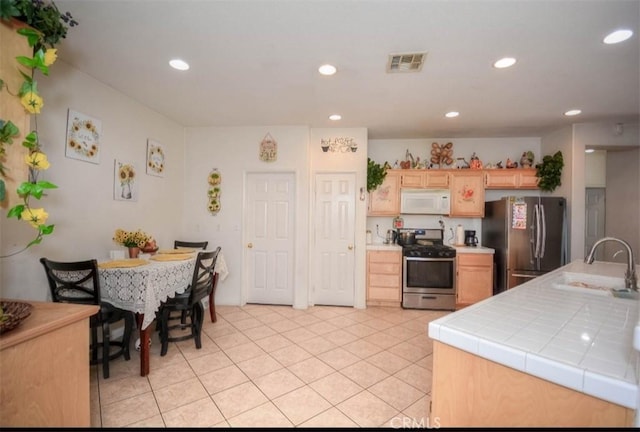 kitchen featuring sink, appliances with stainless steel finishes, light tile patterned flooring, light brown cabinetry, and tile countertops