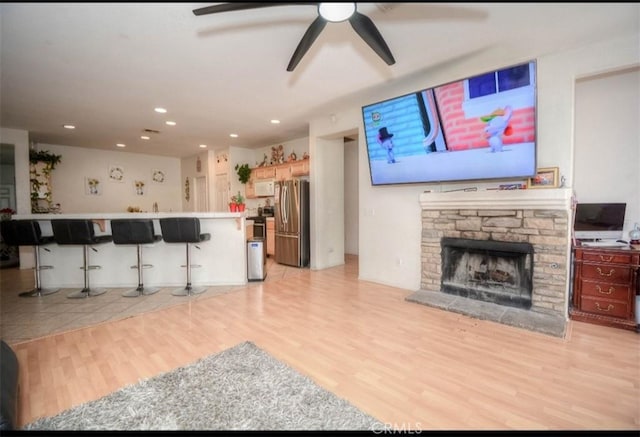 living room featuring ceiling fan, a stone fireplace, and light wood-type flooring