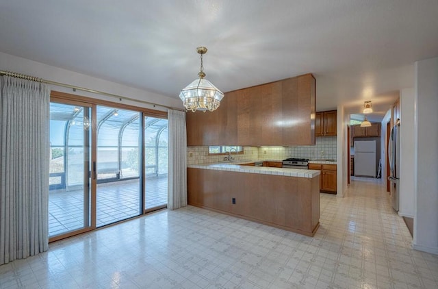 kitchen featuring kitchen peninsula, hanging light fixtures, sink, backsplash, and stainless steel appliances