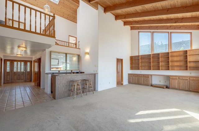 unfurnished living room featuring wooden ceiling, a high ceiling, light colored carpet, and built in desk