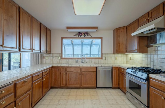 kitchen featuring appliances with stainless steel finishes, decorative backsplash, sink, kitchen peninsula, and tile countertops