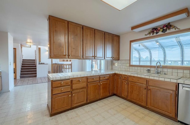 kitchen featuring tasteful backsplash, dishwasher, sink, kitchen peninsula, and tile countertops