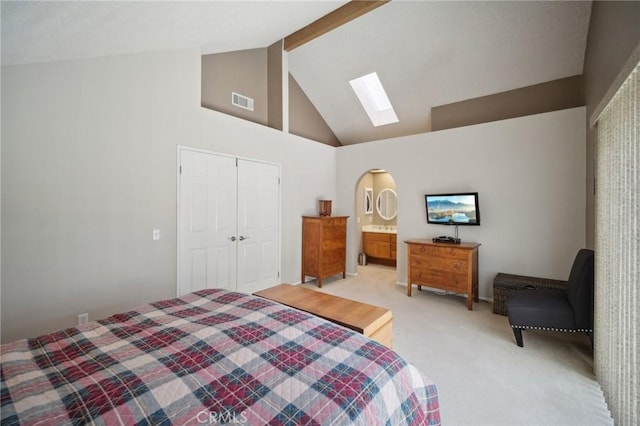 carpeted bedroom featuring a skylight, beamed ceiling, a closet, high vaulted ceiling, and ensuite bathroom