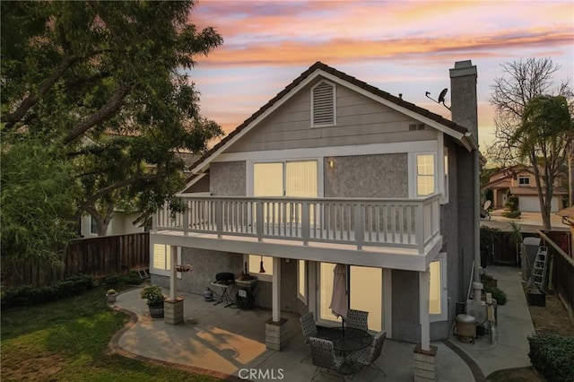 back house at dusk with a balcony and a patio