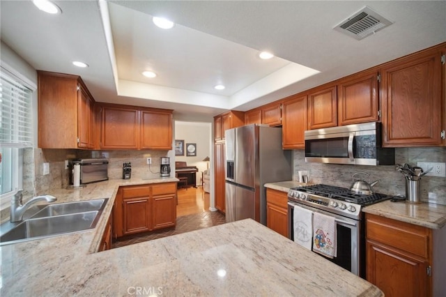 kitchen featuring sink, appliances with stainless steel finishes, decorative backsplash, and a tray ceiling