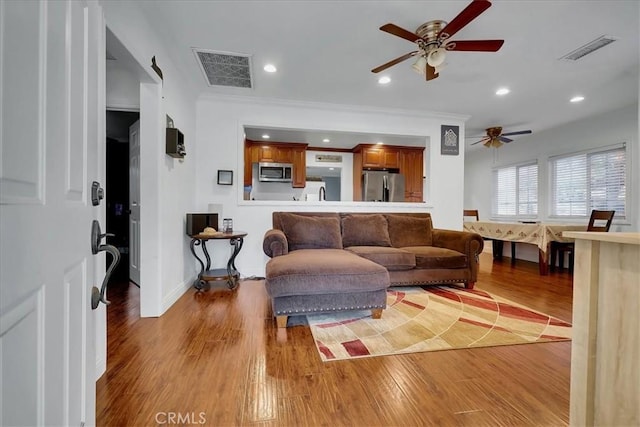 living room featuring ceiling fan, ornamental molding, and light hardwood / wood-style floors