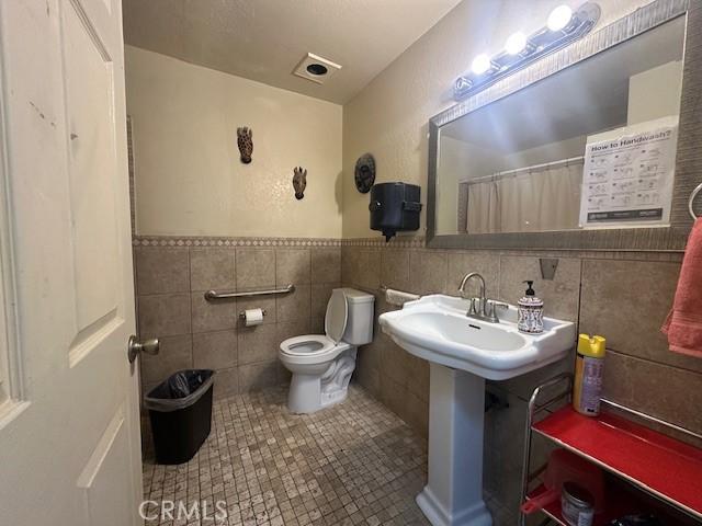 bathroom featuring toilet, tile patterned floors, curtained shower, and tile walls