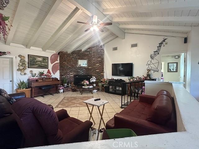 tiled living room featuring ceiling fan, beamed ceiling, a fireplace, and high vaulted ceiling