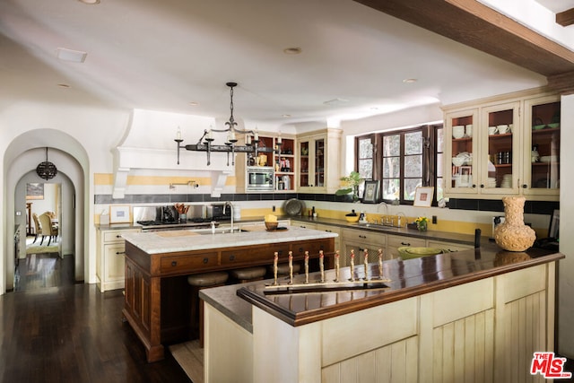 kitchen featuring sink, dark hardwood / wood-style flooring, hanging light fixtures, and an island with sink