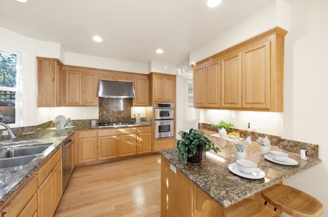 kitchen with appliances with stainless steel finishes, sink, dark stone counters, light hardwood / wood-style floors, and kitchen peninsula