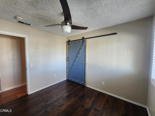 unfurnished room with ceiling fan, a barn door, dark wood-type flooring, and a textured ceiling