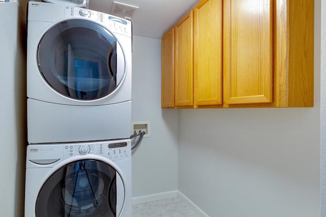 laundry area with stacked washer / dryer, cabinets, and light tile patterned flooring