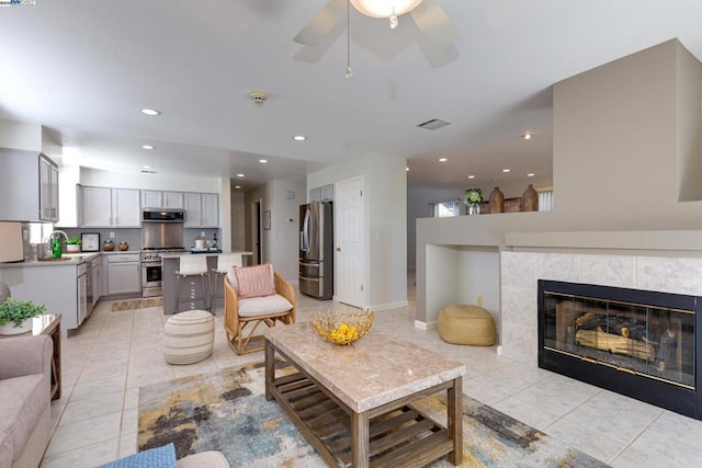 living room with ceiling fan, sink, a tiled fireplace, and light tile patterned flooring