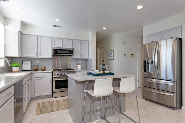 kitchen with appliances with stainless steel finishes, a center island, sink, light tile patterned floors, and a breakfast bar area