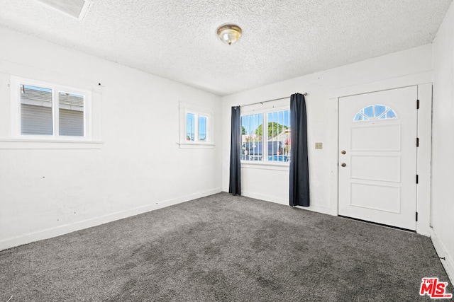 entryway with dark colored carpet and a textured ceiling