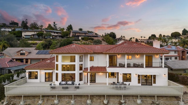 back house at dusk featuring a balcony, an outdoor living space, and a patio area