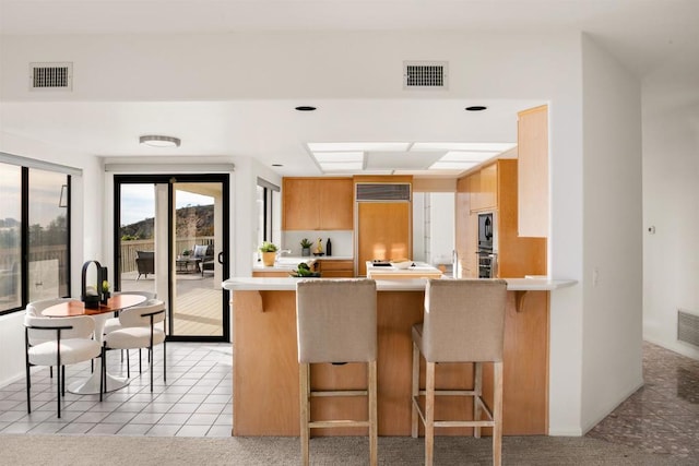 kitchen with black microwave, a kitchen breakfast bar, kitchen peninsula, light colored carpet, and oven