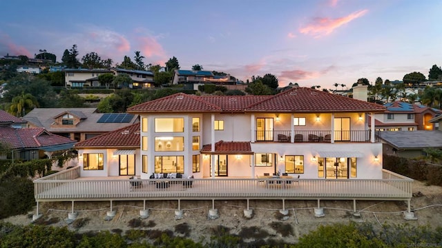 back house at dusk featuring a patio area and a balcony