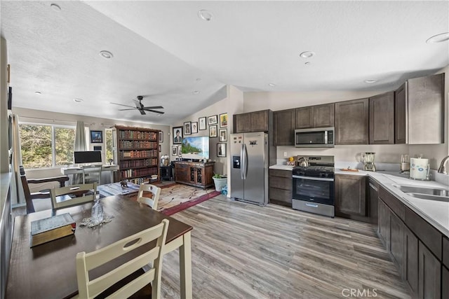 kitchen with sink, vaulted ceiling, dark brown cabinets, light wood-type flooring, and stainless steel appliances