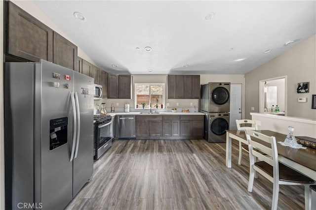 kitchen with sink, stacked washing maching and dryer, appliances with stainless steel finishes, dark brown cabinets, and light hardwood / wood-style floors