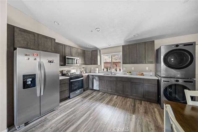 kitchen featuring sink, stacked washing maching and dryer, stainless steel appliances, dark brown cabinetry, and light wood-type flooring