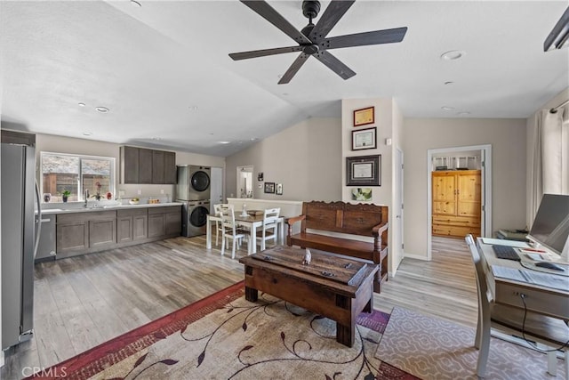 living room featuring stacked washer and dryer, vaulted ceiling, ceiling fan, and light wood-type flooring