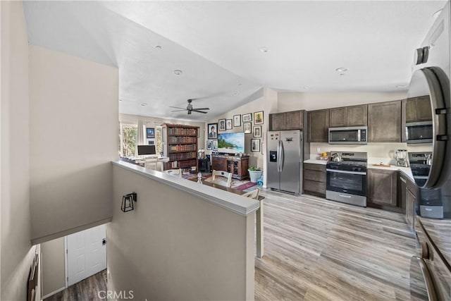 kitchen with vaulted ceiling, dark brown cabinets, kitchen peninsula, stainless steel appliances, and light hardwood / wood-style floors