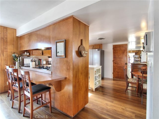 kitchen featuring light wood-type flooring, kitchen peninsula, a breakfast bar, and stainless steel fridge