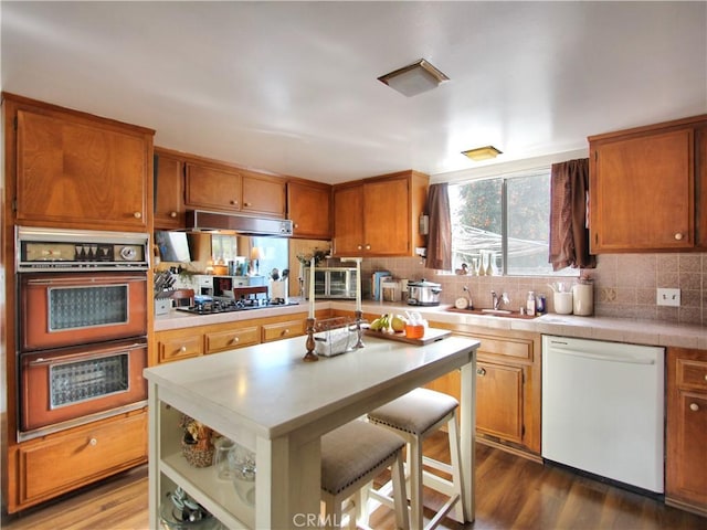 kitchen with white dishwasher, sink, dark hardwood / wood-style floors, double wall oven, and stainless steel gas cooktop