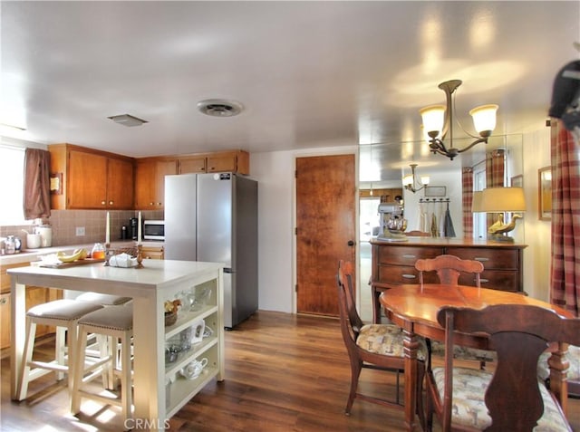 kitchen with hardwood / wood-style floors, decorative backsplash, hanging light fixtures, a chandelier, and stainless steel refrigerator