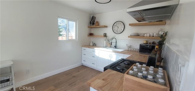 kitchen with extractor fan, black range oven, sink, white cabinets, and light hardwood / wood-style flooring