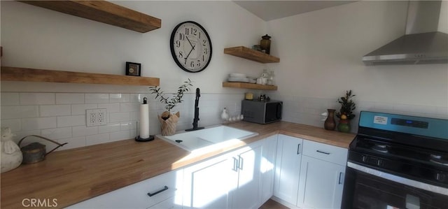 kitchen featuring wall chimney exhaust hood, sink, butcher block countertops, white cabinetry, and black range with electric stovetop