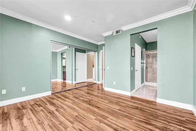 unfurnished bedroom featuring a closet, hardwood / wood-style flooring, ornamental molding, and ensuite bath