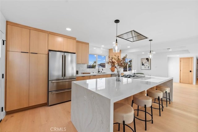 kitchen with a spacious island, pendant lighting, stainless steel appliances, light brown cabinetry, and light hardwood / wood-style flooring