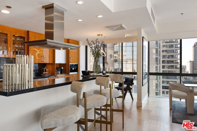 kitchen featuring a wealth of natural light, kitchen peninsula, island range hood, and tasteful backsplash